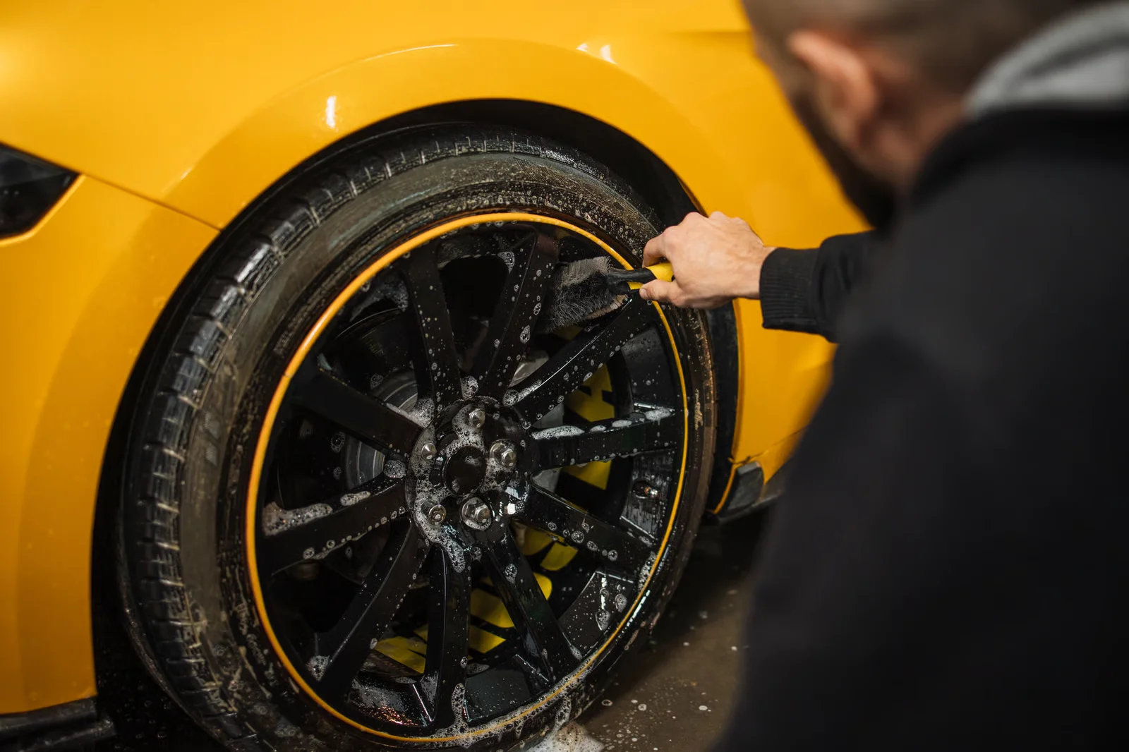 car detailing specialist hand washing the rims and tires of a yellow car