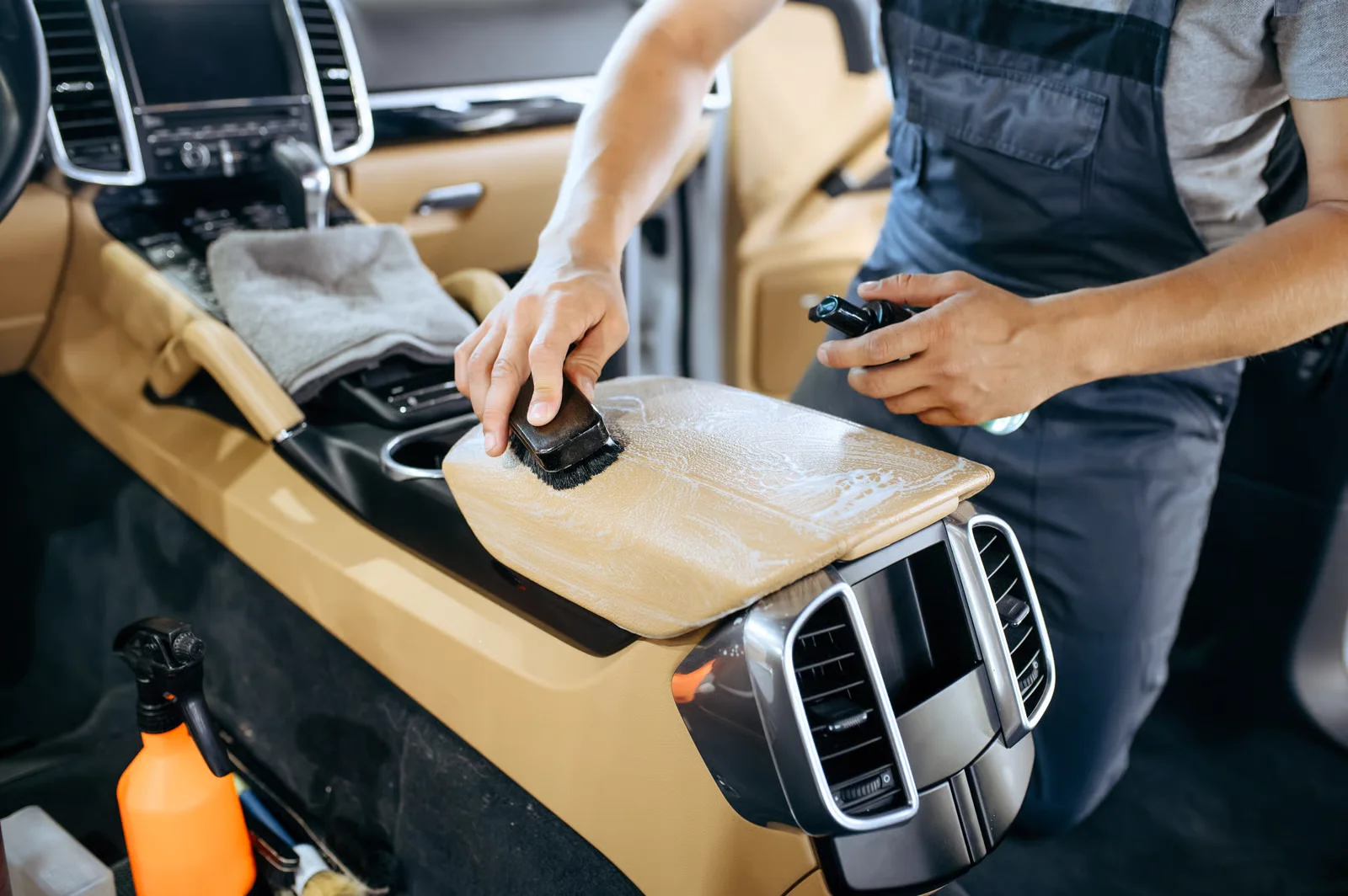 detailing specialist carefully cleaning the beige leather on the armrest of a luxury vehicle