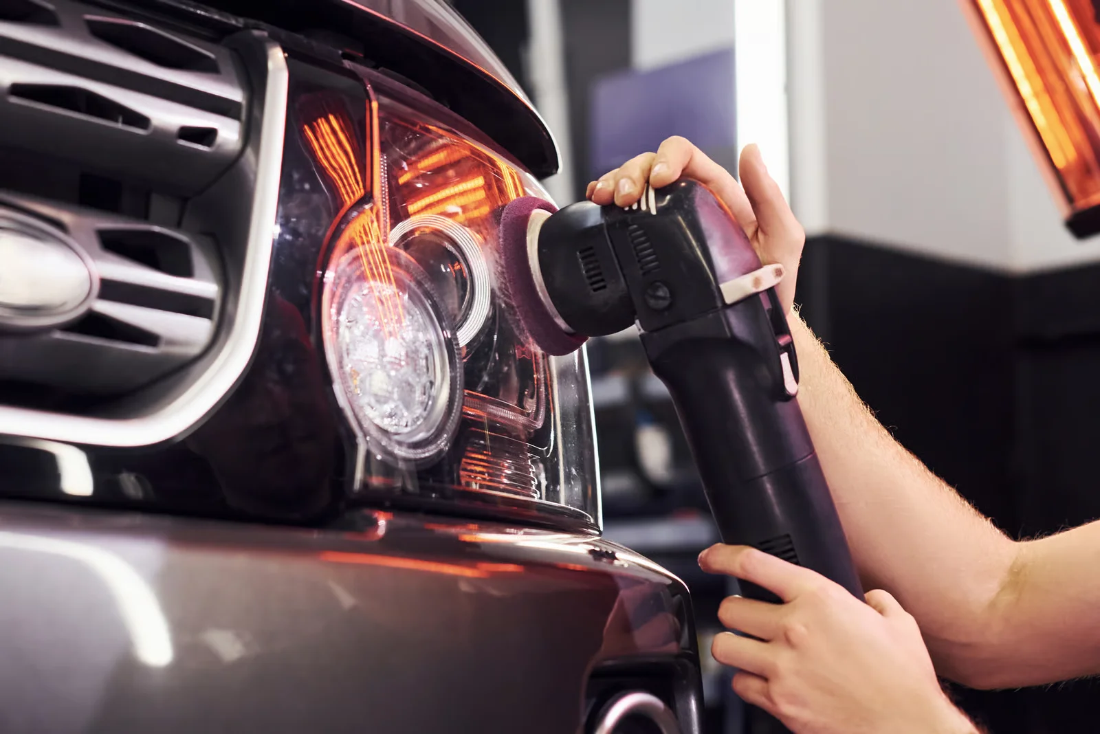 car technician polishing the headlight glass of an SUV to it's original clarity and shine