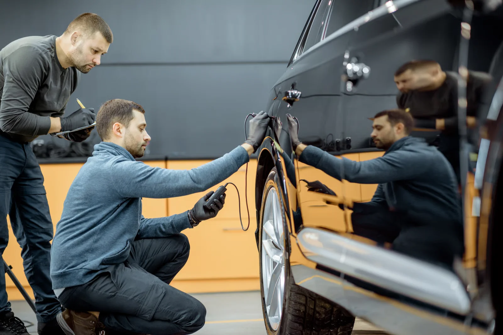 auto mechanics inspecting black car at body shop