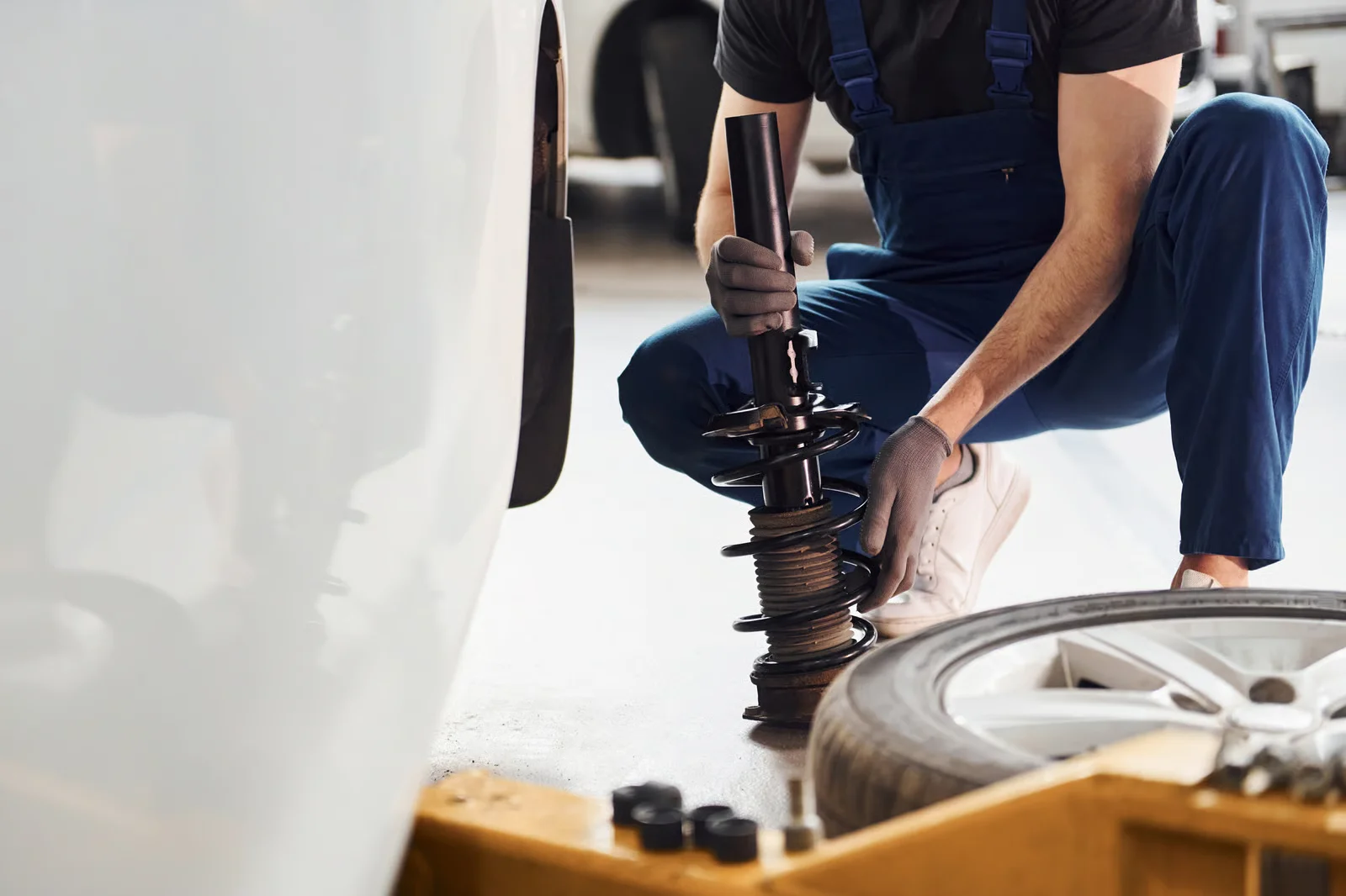 close up view of man in work uniform that repairs white automobile indoors