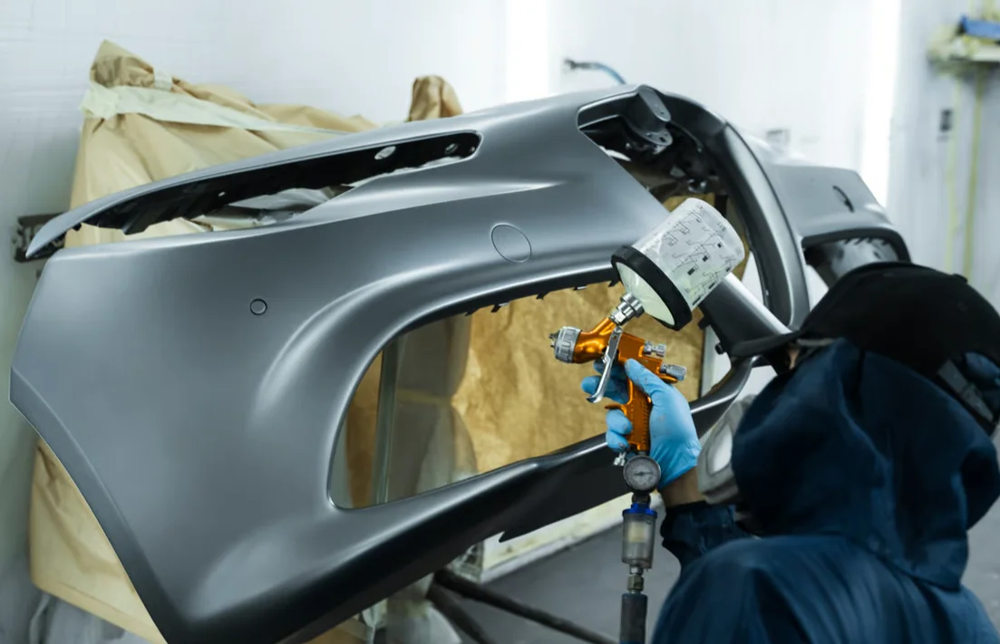 auto body technician painting a bumper in shop