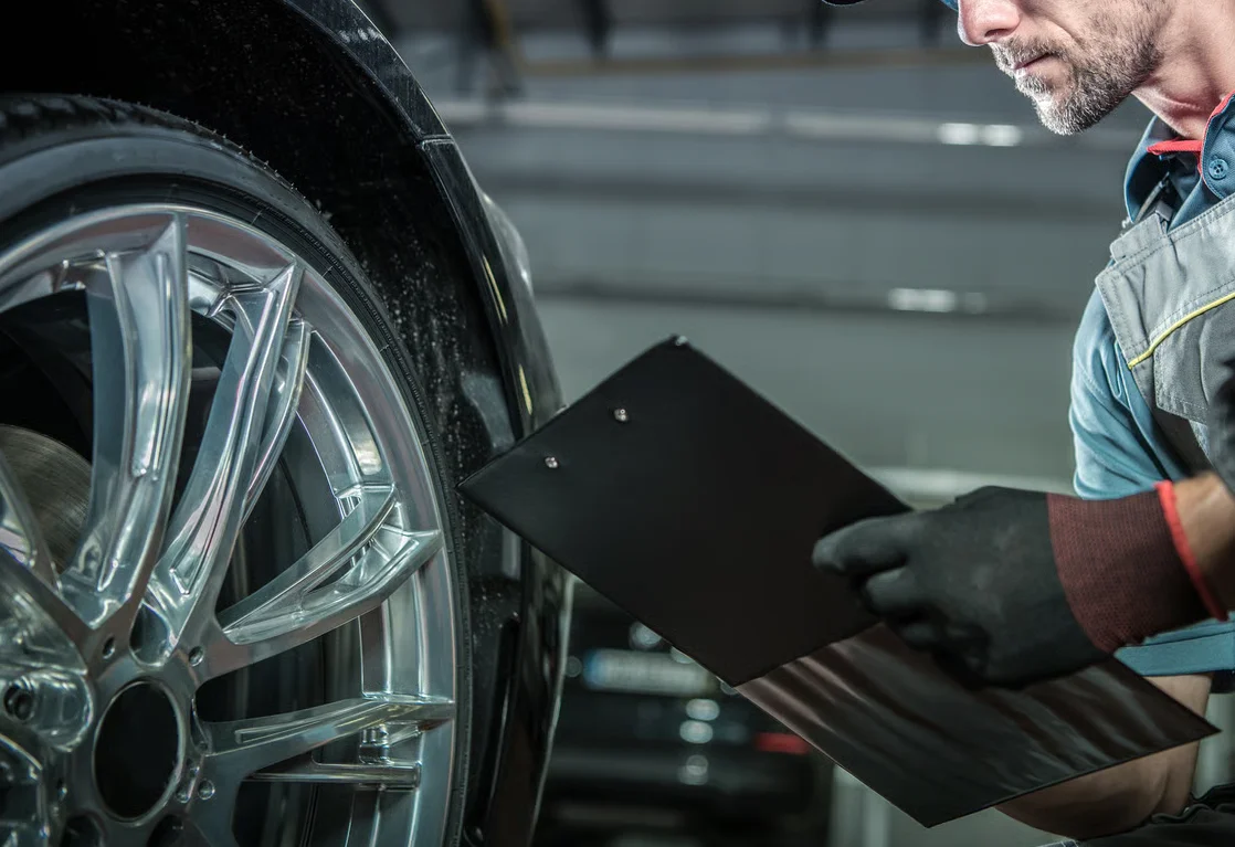 mechanic inspecting wheel with clipboard in auto repair shop