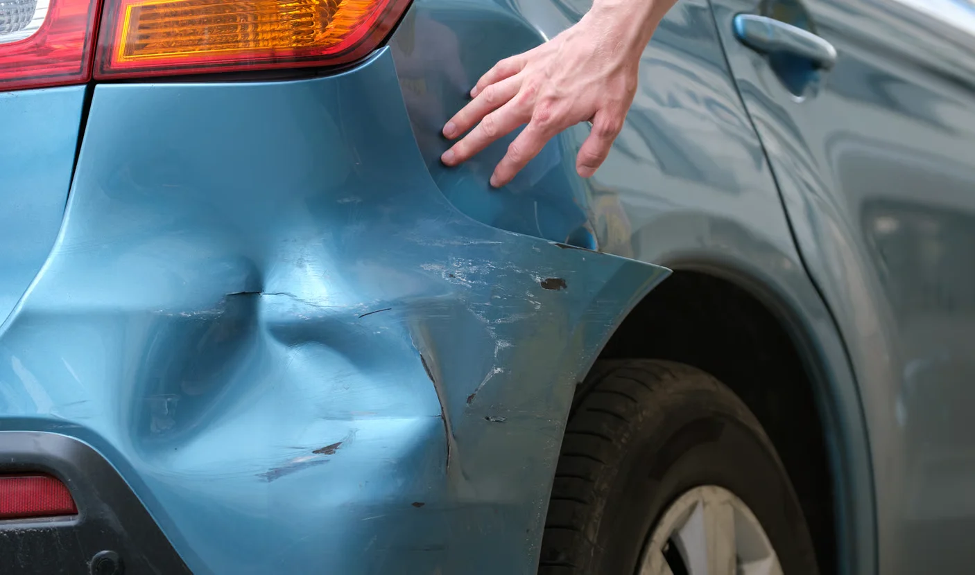 technician hand-examining dented car bumper in auto body shop