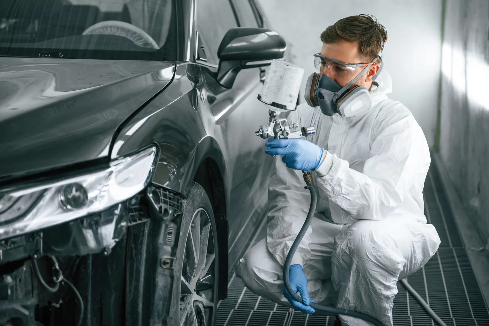 man in paints car in auto body shop paint booth
