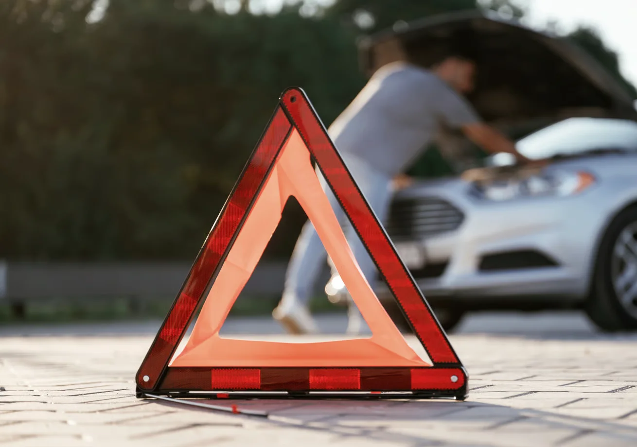 warning triangle on pavement near broken down car after car accident
