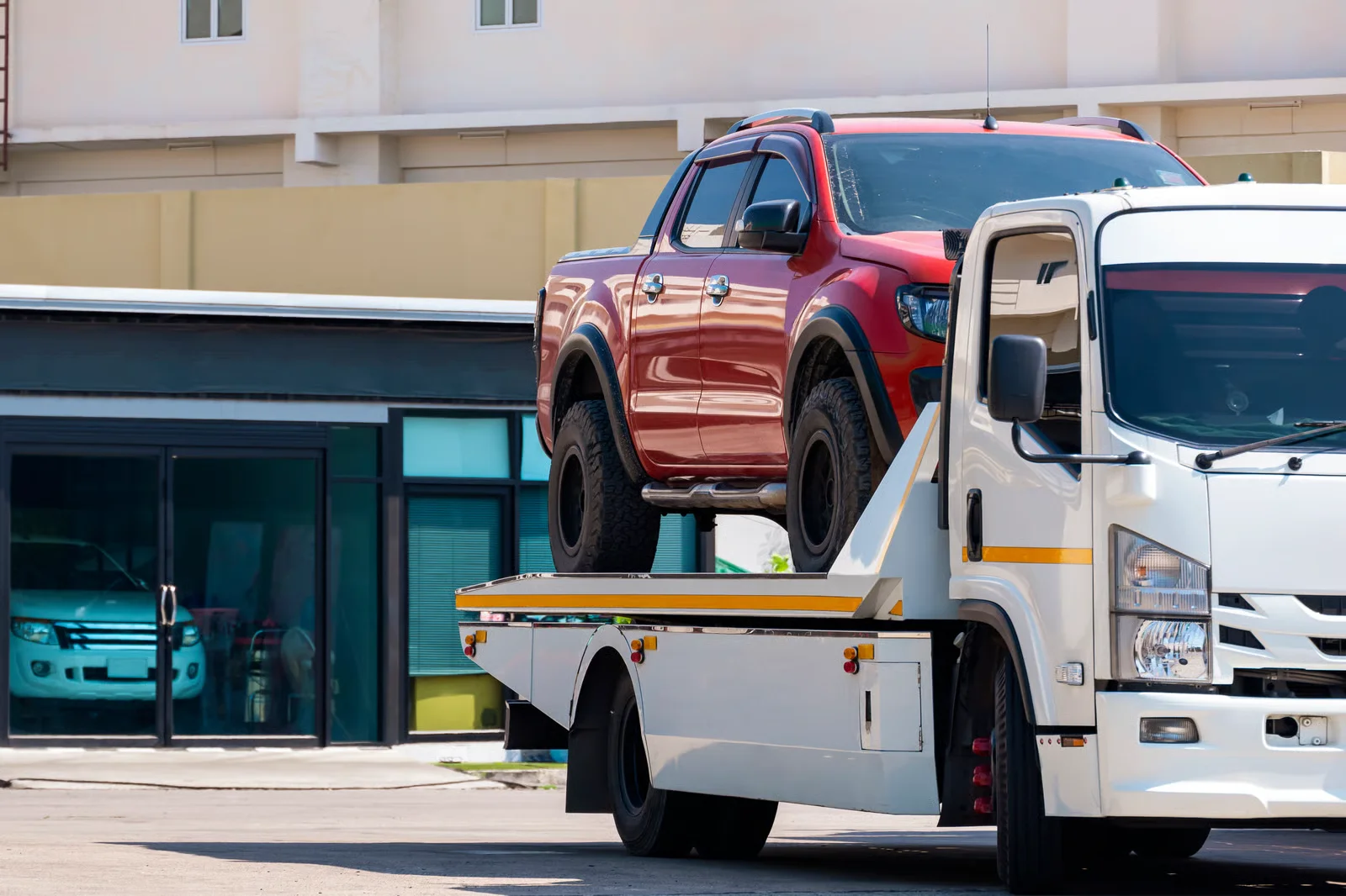 broken red pickup car loaded onto white towing truck in public area for transportation to garage